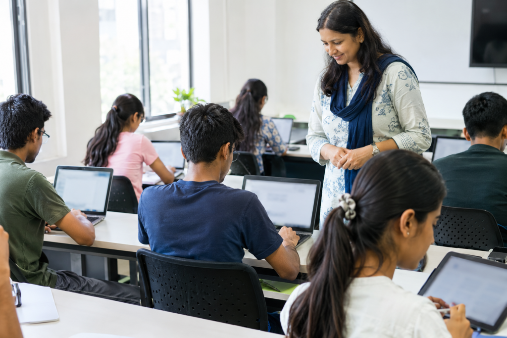 Teacher guiding students working on laptops in a modern classroom